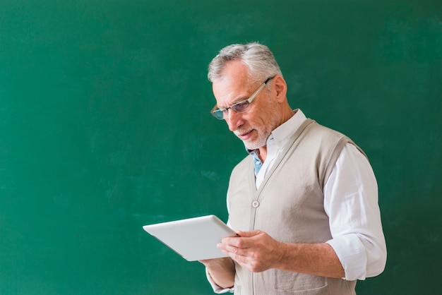 Senior professor masculino usando tablet perto de lousa