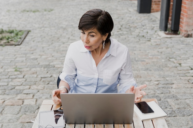 Senior sentado ao ar livre com o laptop tiro médio