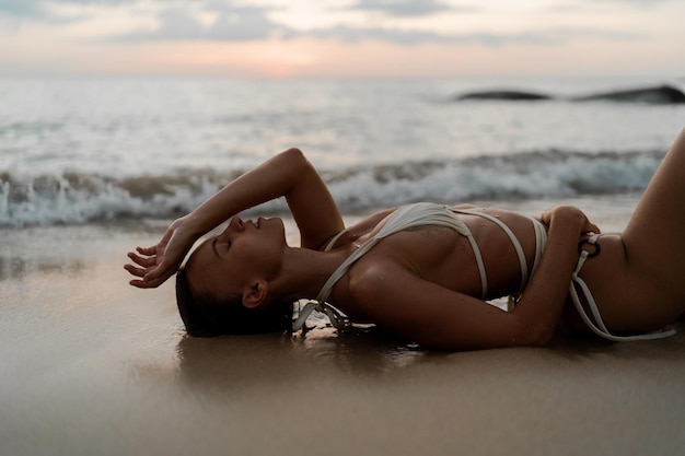 Foto grátis sensual mulher loira deitada na praia de verão. corpo bronzeado perfeito. luz do pôr do sol.