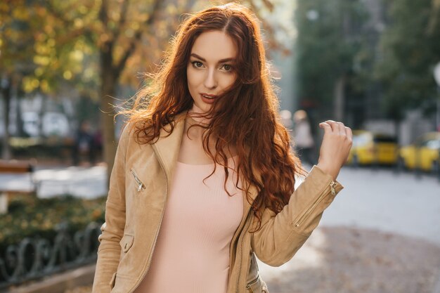 Sensual mulher ruiva com camisa rosa posando na parede natural