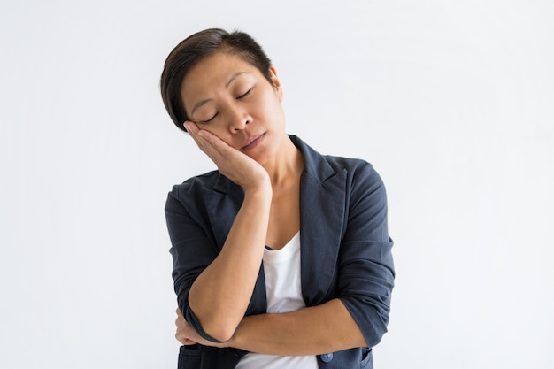 Serena mulher asiática fazendo gesto de sono com os olhos fechados