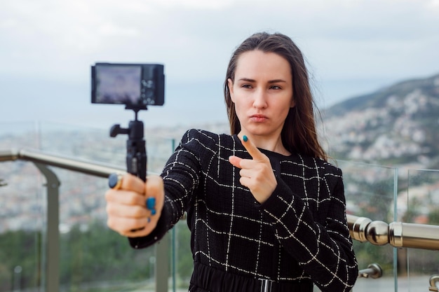 Sério, a garota blogueira está tirando selfie apontando o foco da câmera com o dedo indicador no fundo da vista da cidade