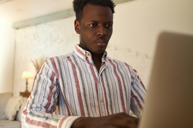 Sério concentrado jovem freelancer afro-americano digitando no laptop, trabalhando em casa. aluno focado na aprendizagem online usando dispositivo eletrônico, passando no teste. tecnologia, educação e trabalho