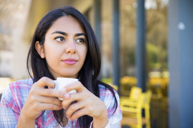 Sério, mulher jovem e bonita desfrutando de beber café no café