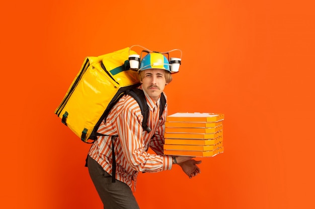 Serviço de entrega sem contato durante a quarentena. Homem entrega comida e sacolas de compras durante o isolamento. Emoções do entregador isolado em fundo laranja.
