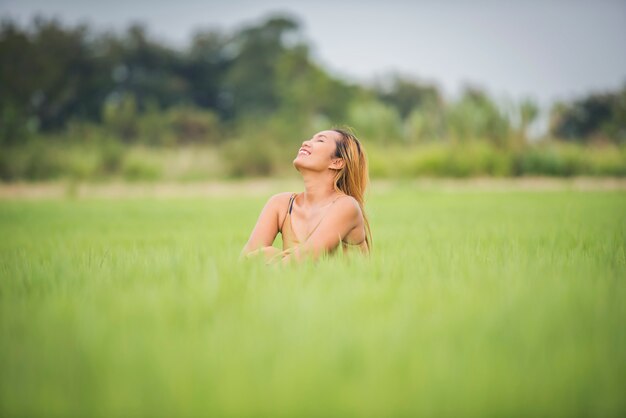 Sessão do assento da jovem mulher boa no campo de grama.