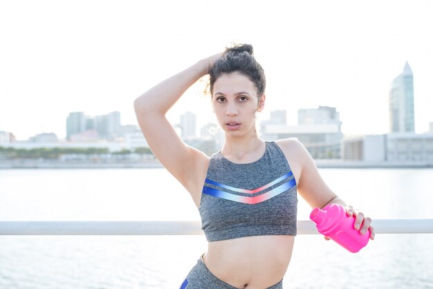 Sexy pretty sporty girl drinking by city river