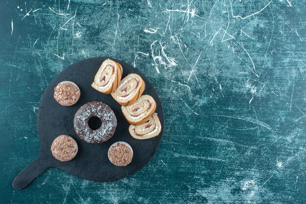 Shortbreads, donut e bolo de rolo fatiado na tábua, na mesa azul.