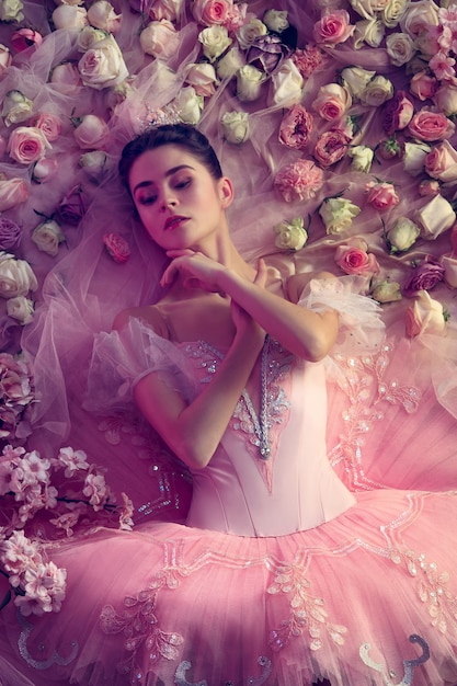 Silêncio é ouro. Vista superior de uma bela jovem em tutu de balé rosa, rodeada por flores. Humor de primavera e ternura à luz coral. Conceito de primavera, flor e despertar da natureza.