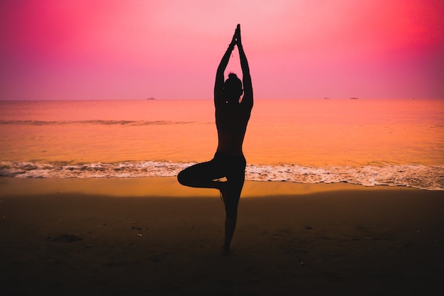Silhueta da mulher que faz a ioga em uma praia