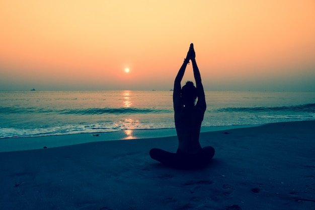 Silhueta da mulher que faz a ioga em uma praia