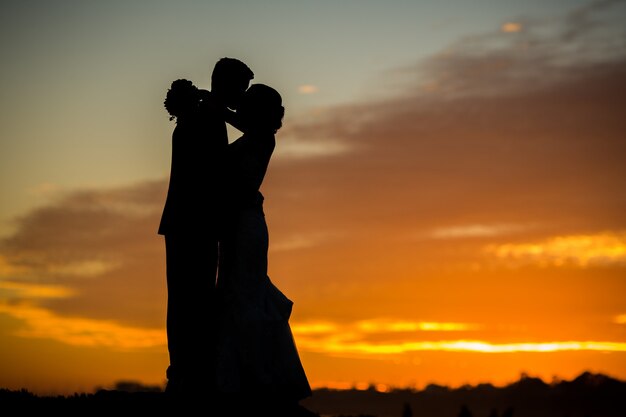 Silhueta da noiva e do noivo se beijando durante o pôr do sol