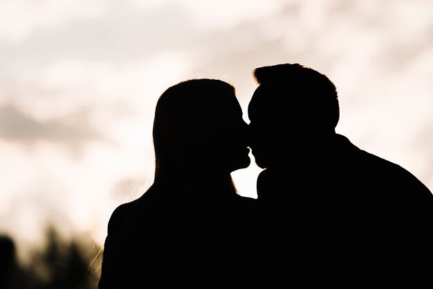 Silhueta de casal contra o céu beijando uns aos outros