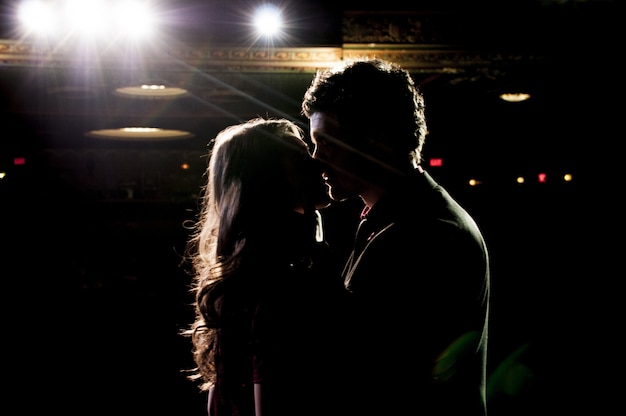Silhueta de casal se beijando em pé no palco do teatro