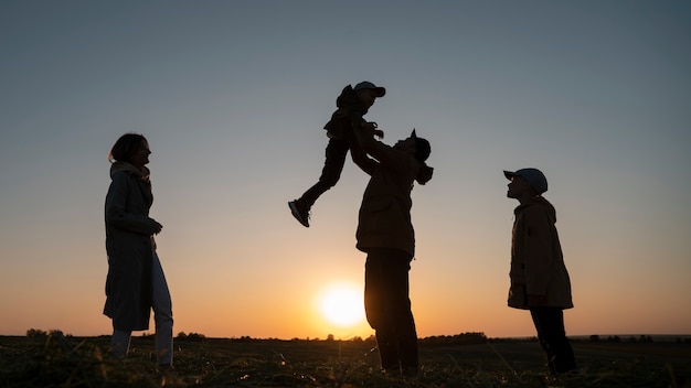 Silhueta de família de tiro completo se divertindo ao pôr do sol