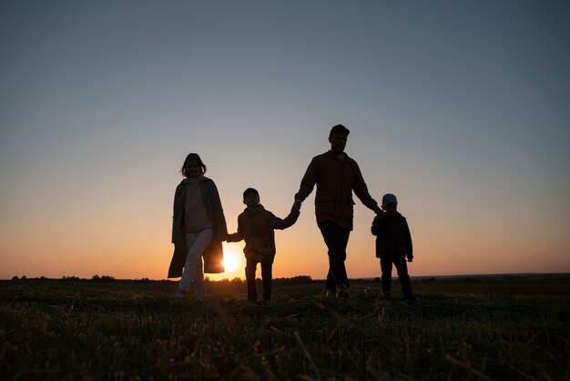 Silhueta de família de tiro completo se divertindo ao pôr do sol