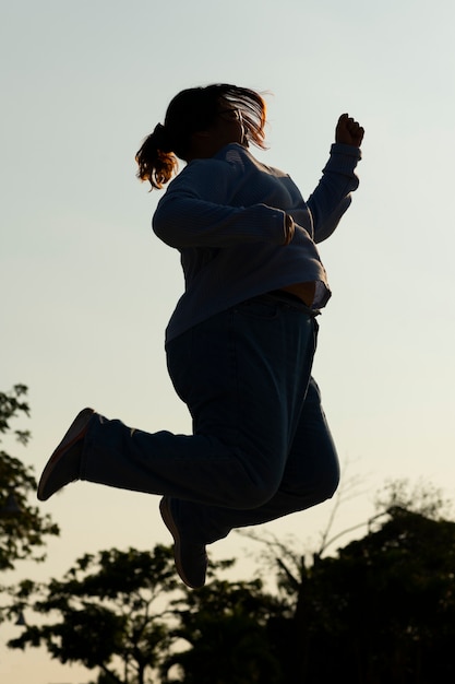 Silhueta de mulher de tiro completo pulando ao pôr do sol
