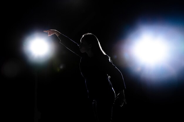 Silhueta de mulher jovem gesticulando isolada na parede preta com lanternas. Copyspace.