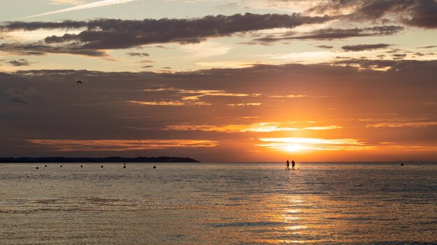 Silhueta de pessoas praticando paddleboard durante o pôr do sol