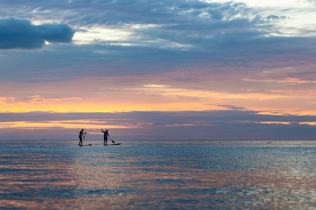 Silhueta de pessoas praticando paddleboard durante o pôr do sol