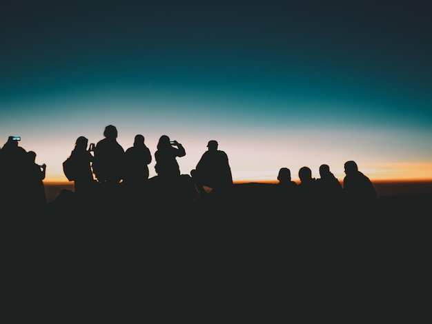 Silhueta de pessoas sentadas e tirando fotos do pôr do sol cênico