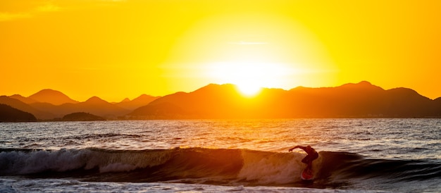 Silhueta de um surfista surfando nas ondas durante o pôr do sol no brasil
