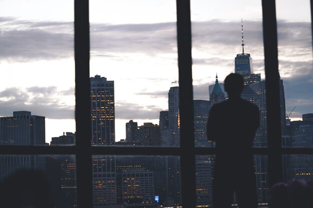 Silhueta de uma bem sucedida posição masculina de uma janela com vista para a ilha de Manhattan