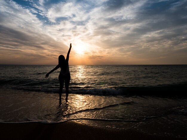 Silhueta de uma jovem na praia. jovem está caminhando ao pôr do sol à beira-mar. Garota de turista de férias na praia.