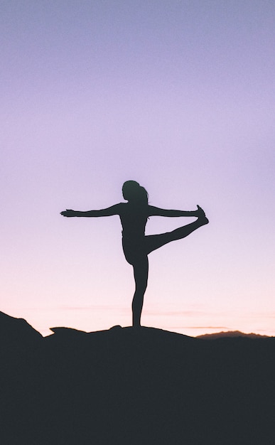 Silhueta de uma mulher em forma praticando ioga em um penhasco alto ao pôr do sol