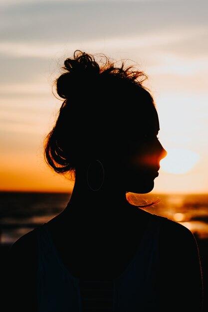Silhueta de uma mulher em pé na costa do mar com um belo pôr do sol
