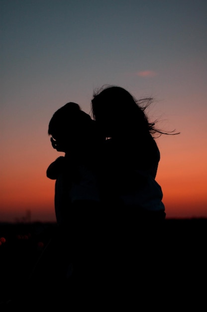 Silhueta do lindo casal abraçado contra o pôr do sol cênico colorido
