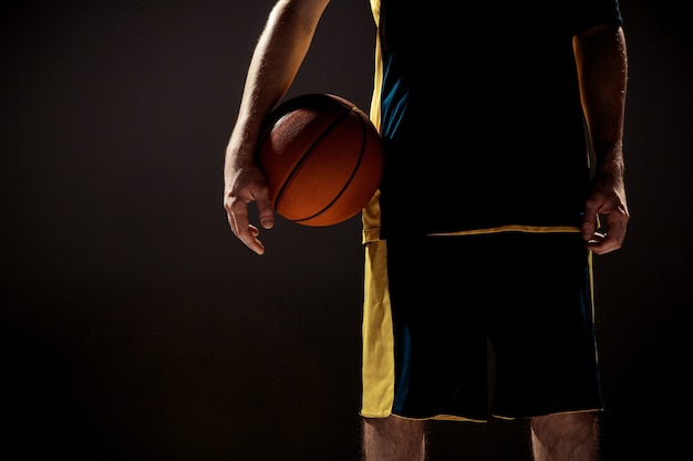 Silhueta, vista de um jogador de basquete, segurando uma bola de basquete na parede preta