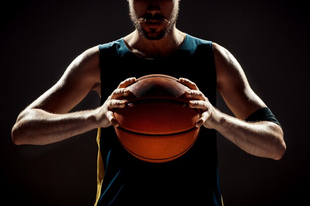 Silhueta, vista de um jogador de basquete, segurando uma bola de basquete no espaço preto