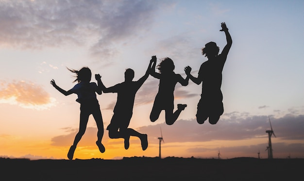 Silhuetas de amigos felizes pulando no pôr do sol