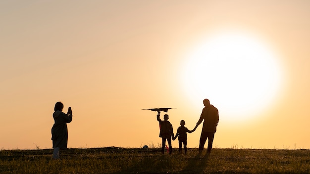 Silhuetas de família se divertindo ao pôr do sol plano completo