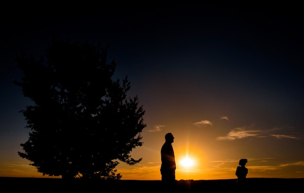 Silhuetas de homem e menina de pé em um campo antes de um por do sol