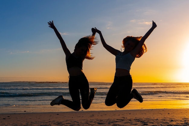 Foto grátis silhuetas de tiro completo de pessoas pulando ao pôr do sol