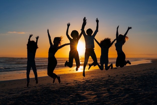 Silhuetas de tiro completo de pessoas pulando ao pôr do sol