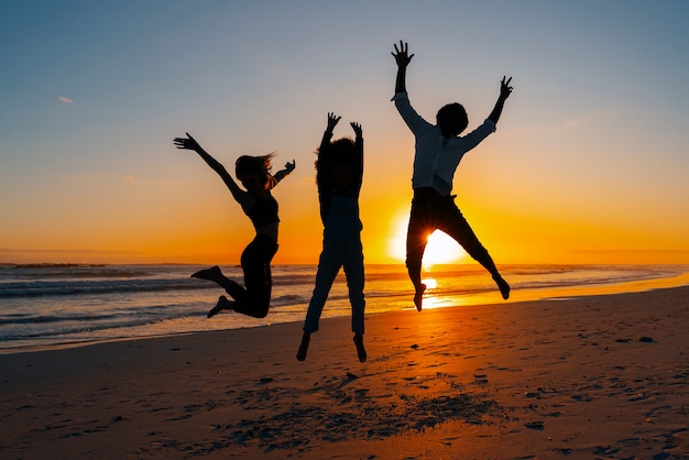 Silhuetas de tiro completo de pessoas pulando ao pôr do sol