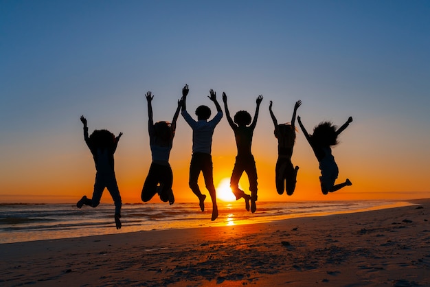 Foto grátis silhuetas de tiro completo de pessoas pulando ao pôr do sol