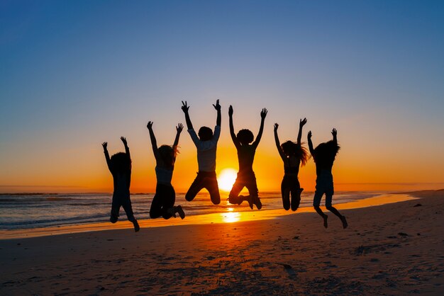 Silhuetas de tiro completo de pessoas pulando ao pôr do sol