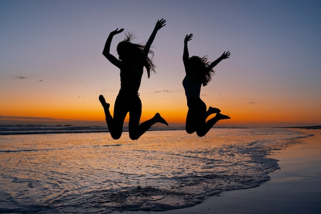 Silhuetas de tiro completo de pessoas pulando ao pôr do sol