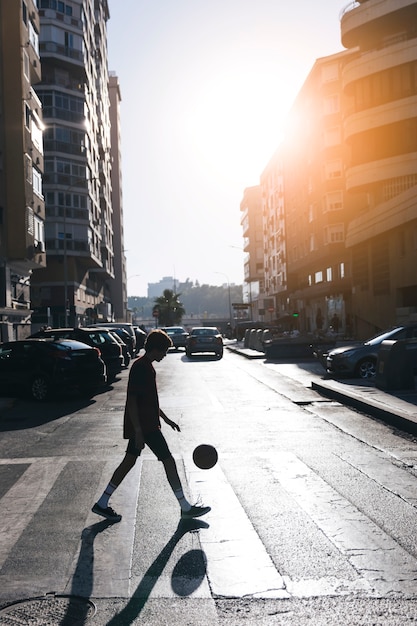Silueta, de, um, menino adolescente, jogando basquetebol, ligado, rua, em, cidade