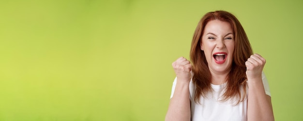 Foto grátis sim, conseguimos. feliz, ruiva de sorte, mulher de meia-idade, vencedora. bomba os punhos para cima. celebração de sucesso.