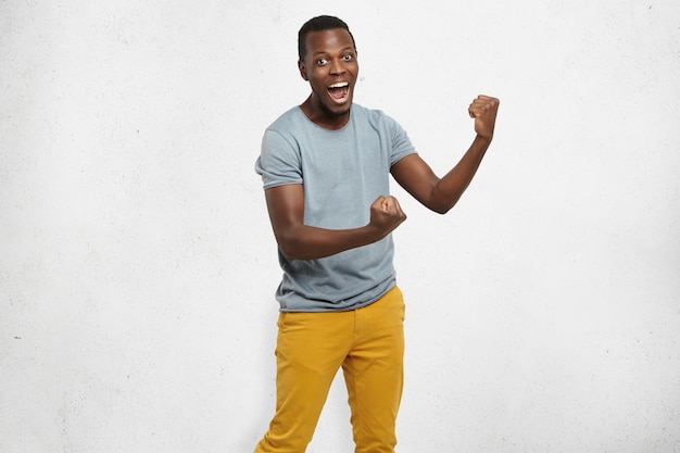 Foto grátis sim! empregado afro-americano jovem e bonito se sentindo animado, gesticulando ativamente, mantendo os punhos cerrados, exclamando alegremente com a boca aberta, feliz com boa sorte ou promoção no trabalho