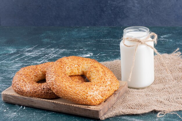 Simit bagels com gergelim e pote de leite em azul.