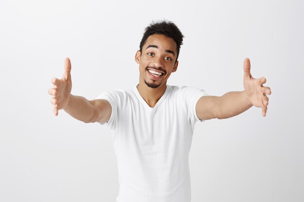 Simpático cara de pele escura estendendo as mãos, segurando algo, abraçando ou dando um abraço