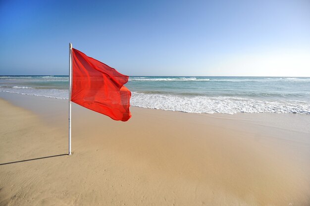 Sinal de alerta de uma bandeira vermelha em uma bela praia com céu azul e mar azul-turquesa