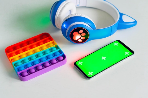 Smartphone com maquete de tela verde em branco com fones de ouvido para crianças e arco-íris pop it fidget