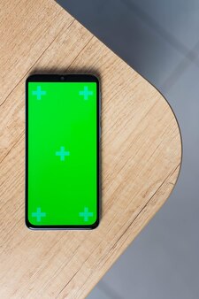 Smartphone com maquete de tela verde em branco sobre fundo de madeira com espaço de cópia